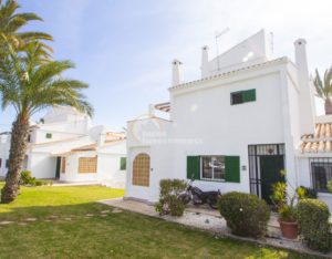 A white semi-detached villa with green shutters and palm trees near Alicante.