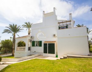 A semi detached villa near Alicante with a white house and green shutters surrounded by palm trees.