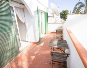 A semi-detached villa near Alicante with a balcony featuring a table and chairs and green shutters.