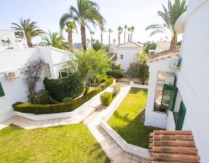 An aerial view of a semi-detached villa with lush green lawn, palm trees near Alicante.
