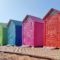 Colorful beach huts for sale on a wooden boardwalk.
