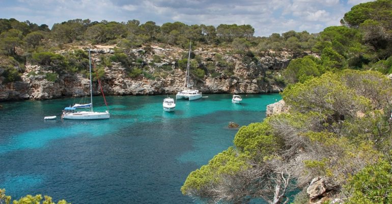 Boats are docked in a Mallorca paradise surrounded by blue Mediterranean water and trees.