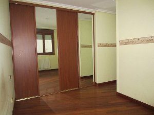 An empty room with wooden floors and a mirror in a 99 m2 apartment in San Sebastian.