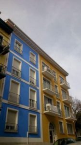 A blue and yellow apartment building in LAREDO with cars parked in front of it.