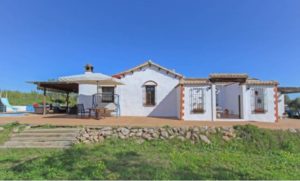 Detached white house with a patio in Coin, situated in a grassy field.