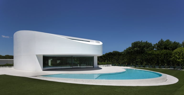 A dream house in Spain featuring a white exterior and a pool in front.