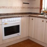 A small kitchen with a stove and microwave in a townhouse for less than 100.000€ in Orihuela Costa.