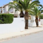 A white townhouse in Villamartin, Orihuela Costa for less than 100.000€ with palm trees in front of it.