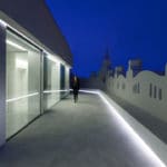 A person walks down a walkway at night in front of a renovated building in Spain.