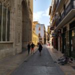 Two people are walking down a narrow street in the city of Valencia.
