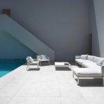 A white sofa and chairs next to a pool.