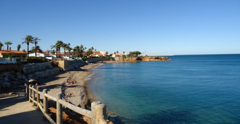 A beach with palm trees and a wooden boardwalk in Spain.