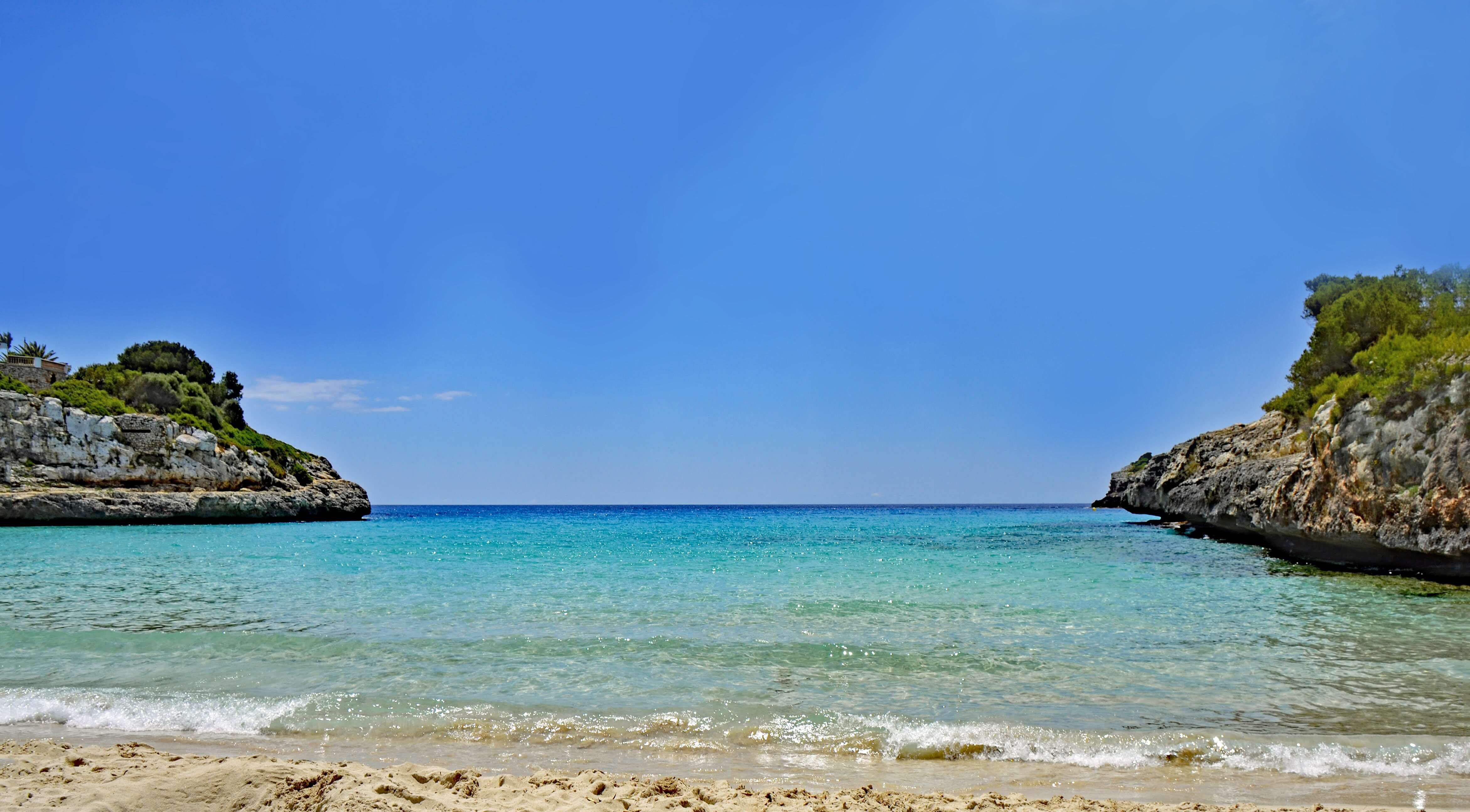 A sandy beach with blue water and a rocky cliff.
