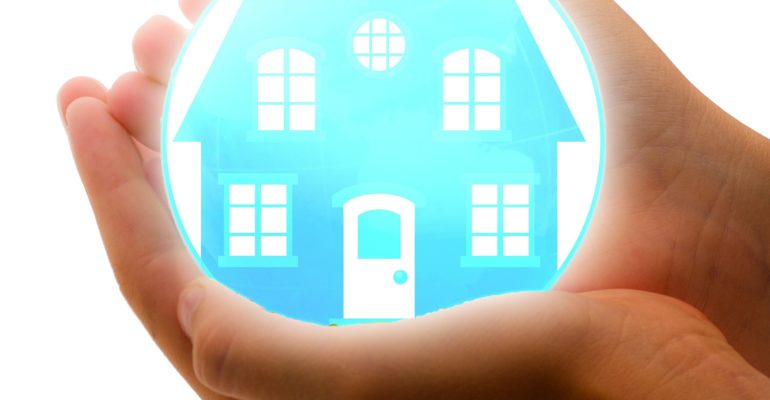 A person's hand holding a blue ball with a house in it, representing holiday home insurance in Spain.