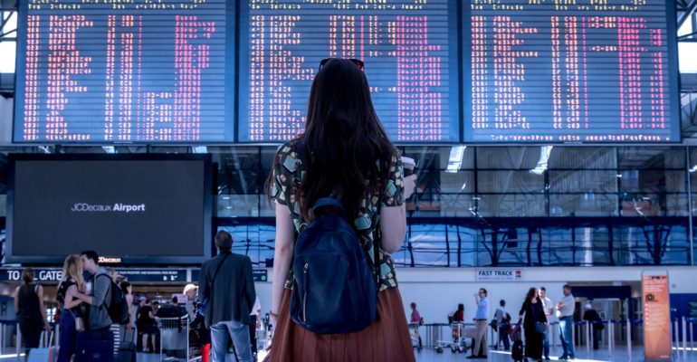 A woman is standing in front of a flight schedule board at an airport, planning her Spain tourism.