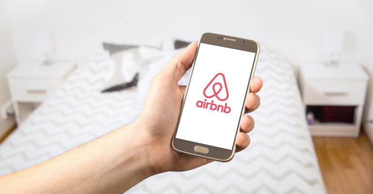 A person holding an Airbnb phone with the Airbnb logo on it, representing short term rental in Spain and addressing concerns about Airbnb's legality in the country.