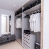 A walk-in closet with clothes and a bench in a San Roque penthouse.
