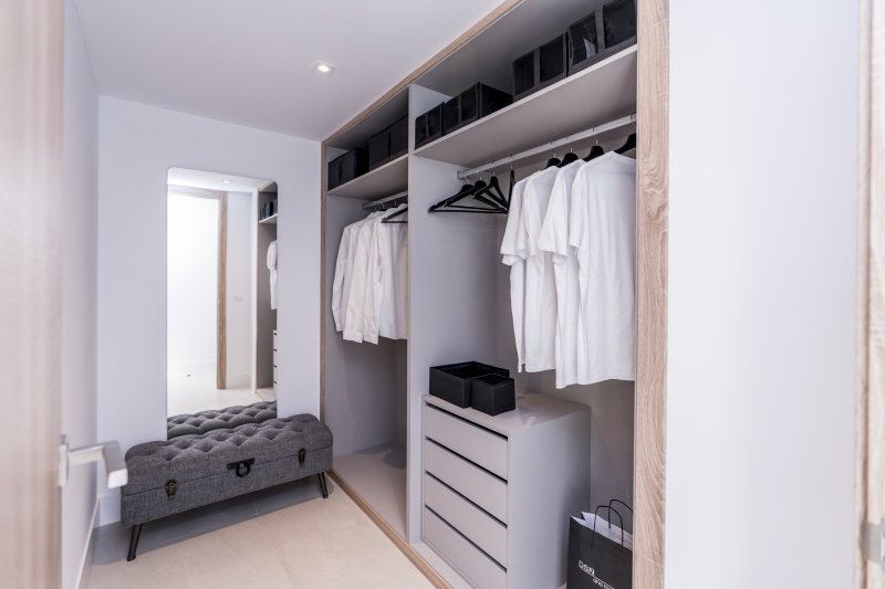 A walk-in closet with clothes and a bench in a San Roque penthouse.