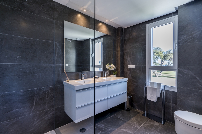 A modern bathroom in a new build penthouse with black walls and a glass shower.