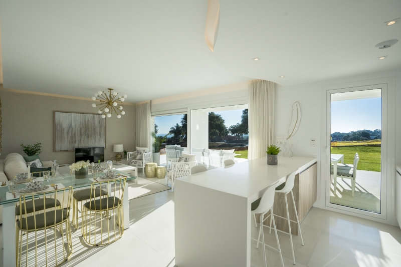 A white kitchen and living room with a view of the golf course in a San Roque New Build apartment.