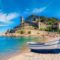 A castle overlooks a boat on the beach in Tossa de Mar, a countryside property in Costa Brava.