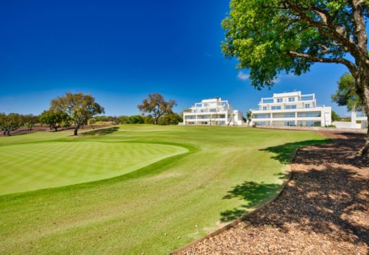 A golf course with trees and buildings in the background, located in Cadiz or San Roque.