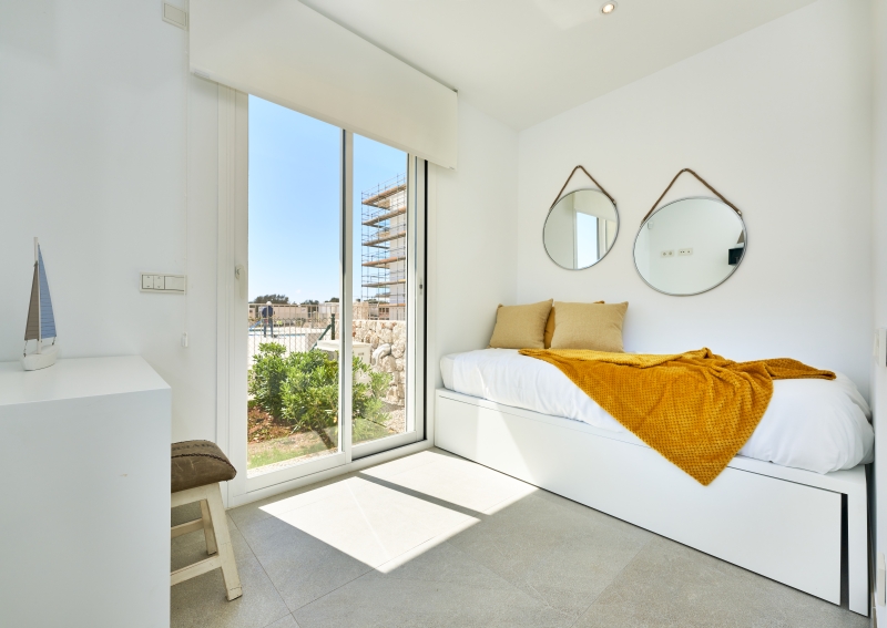 A white bedroom in a new build apartment with a bed and a window.