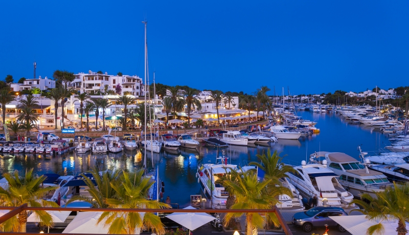 Boats docked in a marina at dusk near a new build apartment in Cala d'Or.
