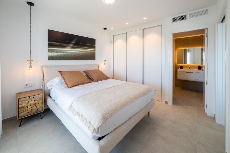 A bedroom with a white bed and a painting on the wall in a Gran Alicante new build apartment.