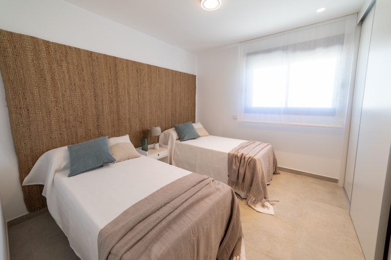 A bedroom with two beds and a wooden wall in a Gran Alicante new build apartment.