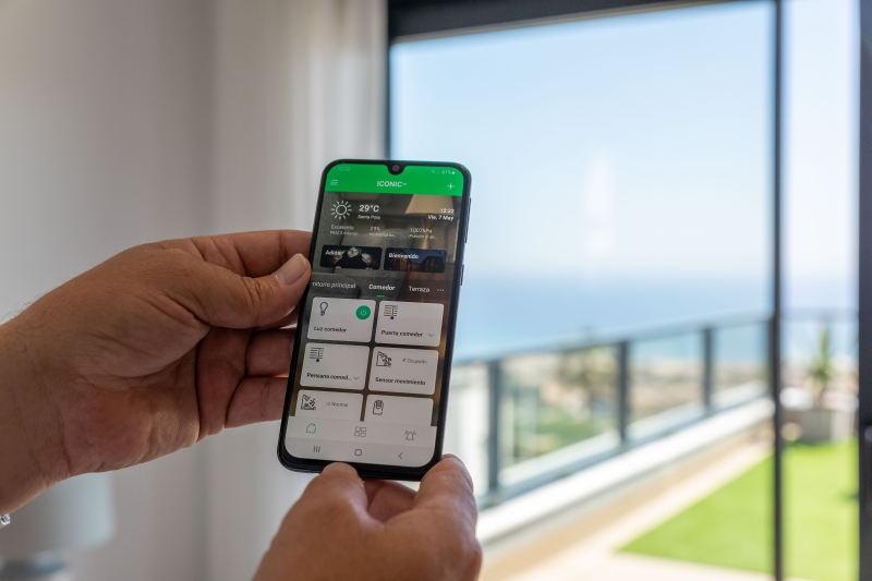 A person holding a smart phone in front of a balcony showcasing Gran Alicante New Build Apartments.