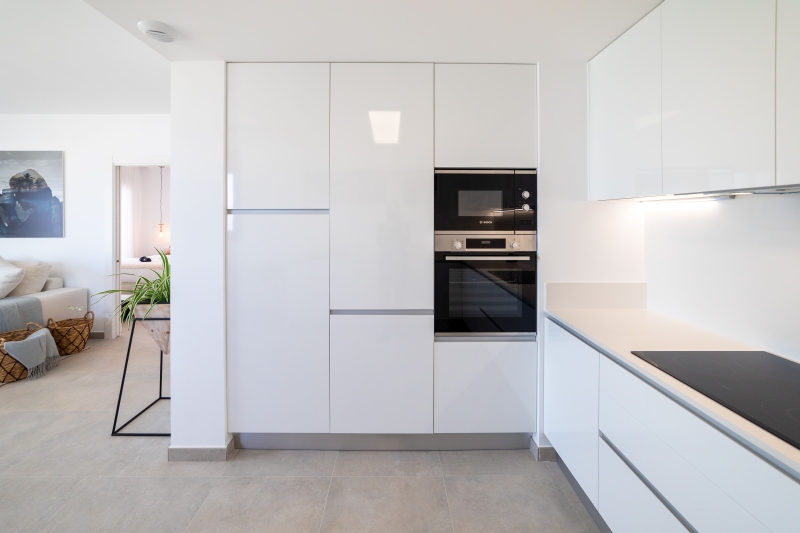 A modern kitchen with white cabinets and a microwave in an Alicante property for sale.
