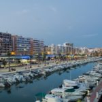 A marina with boats docked in front of buildings at dusk and Alicante property for sale.