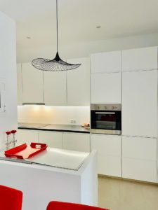 A modern kitchen renovation in Barcelona with red chairs and white cabinets.