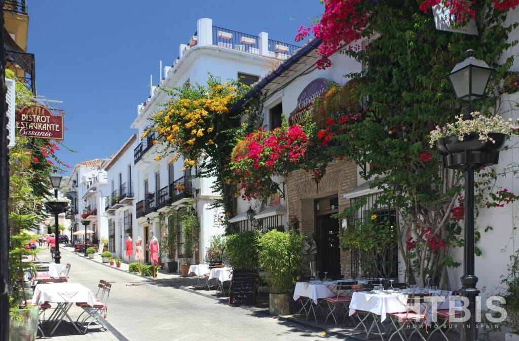 A narrow street with tables and flowers hanging from the trees near a penthouse in Malaga.