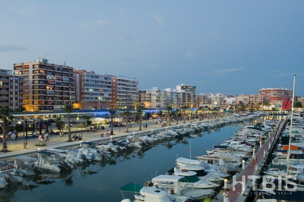 A marina with boats docked in front of buildings, showcasing a Gran Alicante new build apartment.