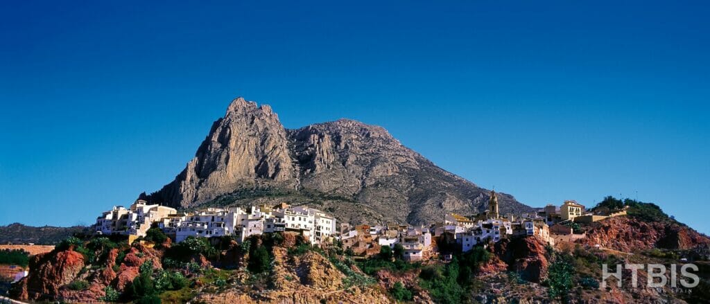 A mountain with a village on top of it, overlooking cheap Alicante property for sale.