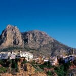 A mountain with a village on top of it, overlooking cheap Alicante property for sale.