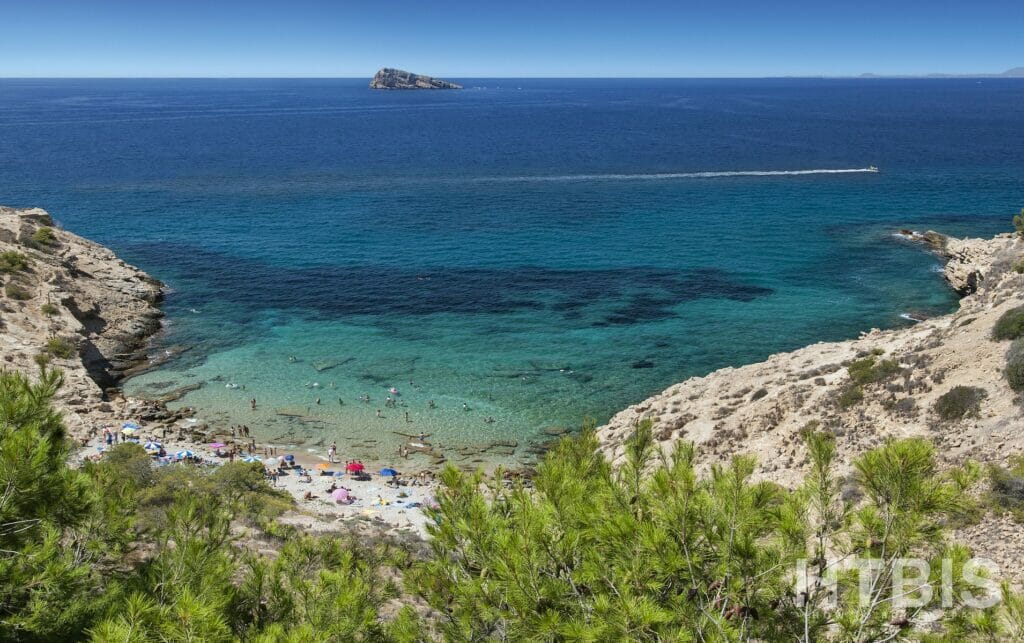 A beach with clear blue water, a rocky cliff, and a view of the cheap Alicante property for sale.