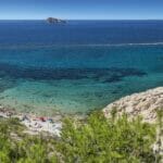 A beach with clear blue water, a rocky cliff, and a view of the cheap Alicante property for sale.