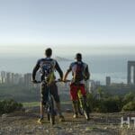 Two mountain bikers standing on top of a mountain overlooking Alicante, with views of the new build apartments and properties for sale.