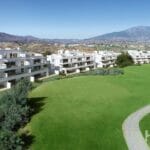 An aerial view of a Marbella New Build apartment complex with a golf course and mountains in the background.