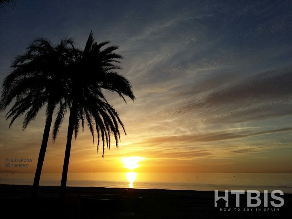 The sun is setting over a beach with palm trees in the background, near the Estepona Golf Course.
