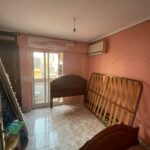 This Costa Dorada property for sale features an empty room with pink walls and a tiled floor. Disassembled bed frames are leaned against the walls, while a sliding glass door opens to a balcony. An air conditioning unit is mounted on the wall, adding modern comfort to this charming space.