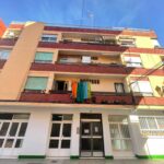 A charming four-story building, perfect for anyone looking for a Costa Dorada property for sale, showcases laundry on its balcony railing. Its brick and stucco facade overlooks the bustling street below on a sunny day.