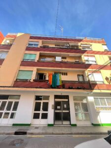 A charming four-story building, perfect for anyone looking for a Costa Dorada property for sale, showcases laundry on its balcony railing. Its brick and stucco facade overlooks the bustling street below on a sunny day.