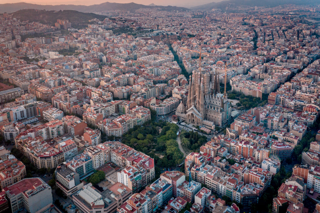 Aerial view of an expansive cityscape in Spain, where a prominent cathedral rises amidst densely packed buildings and lush greenery, captured during sunset. This vibrant scene is popular among travelers seeking temporary rentals and exploring local holiday rental regulations.