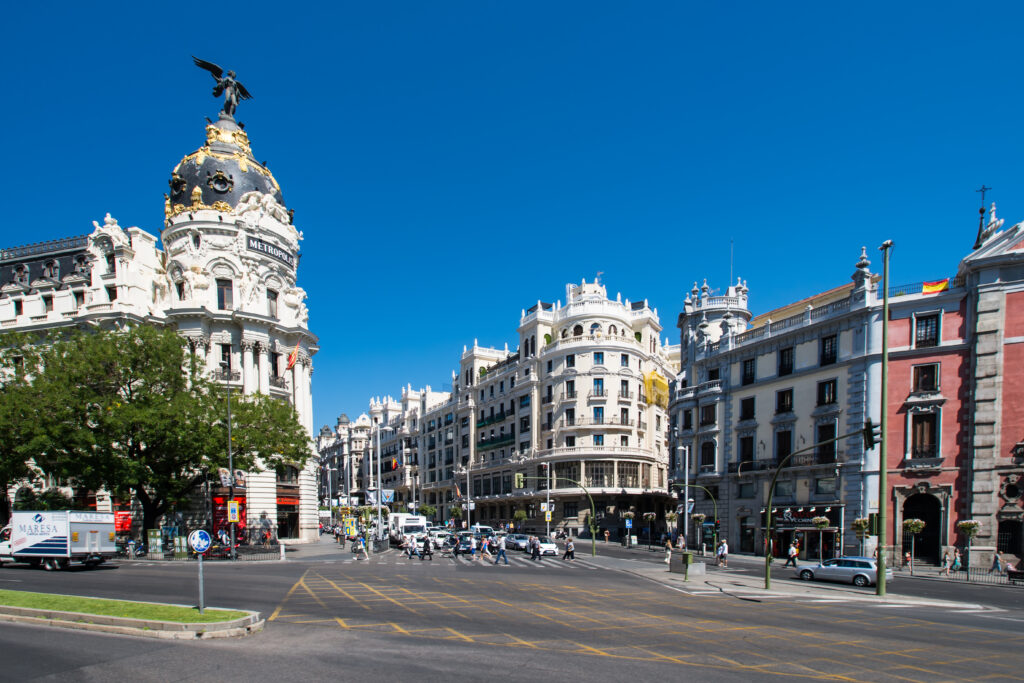 Gran Vía street view in Madrid, featuring the Metropolis Building with its ornate dome under a clear blue sky; a perfect spot to admire while considering temporary rentals in Spain for your next getaway.