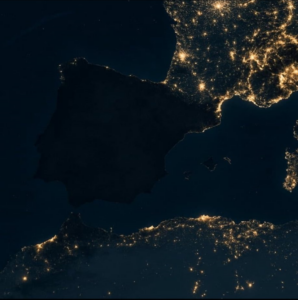 Satellite view of the Iberian Peninsula at night shows Spain and Portugal mostly dark, with brightly lit, France, and coastal North Africa.